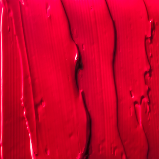 A close-up of a swatch of Karma Matte Lipstick applied to skin, revealing a rich, vibrant red shade with a matte smooth finish.